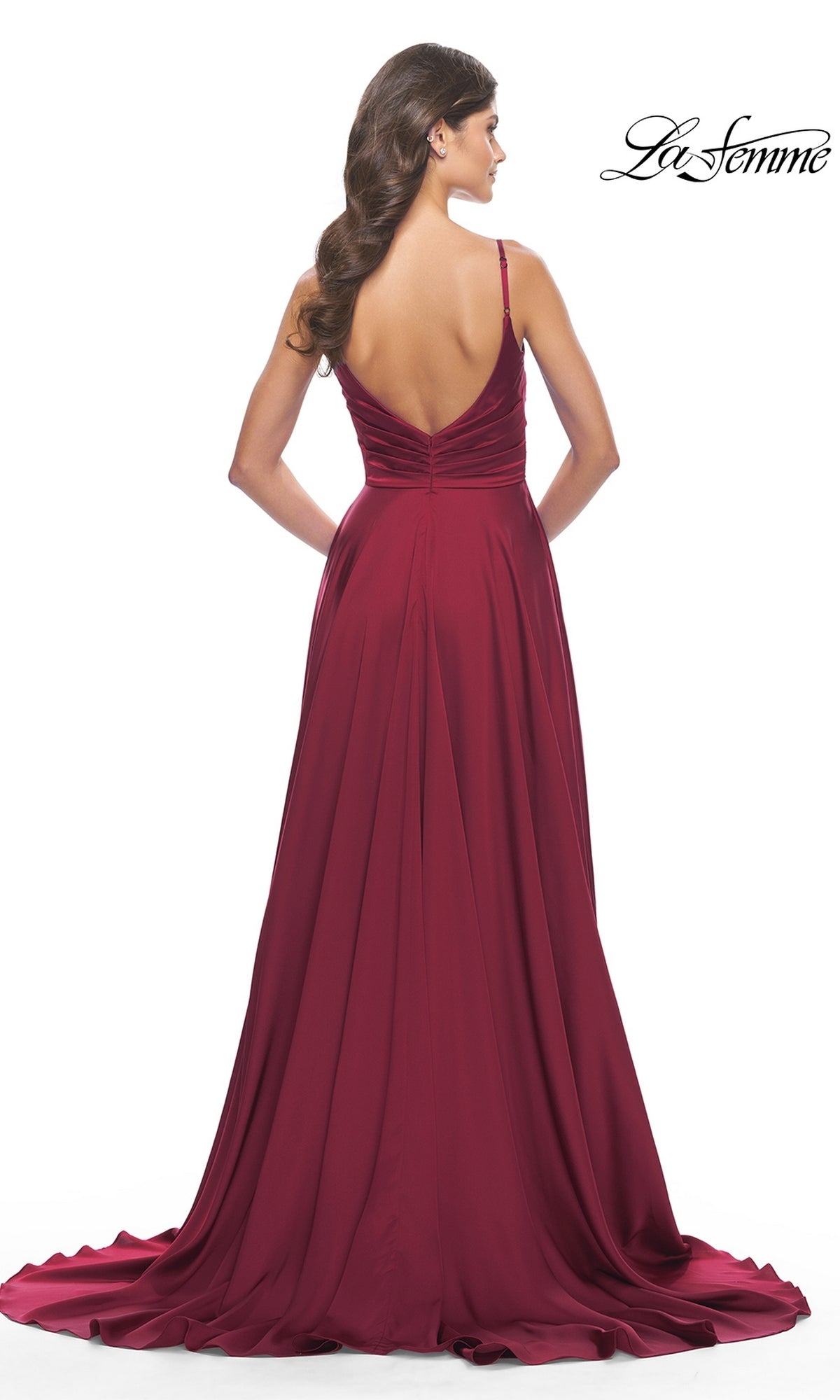A woman stands with her back to the camera in a floor-length, deep red La Femme Open-Back A-Line Designer Prom Dress 31233, featuring thin straps and a low back.